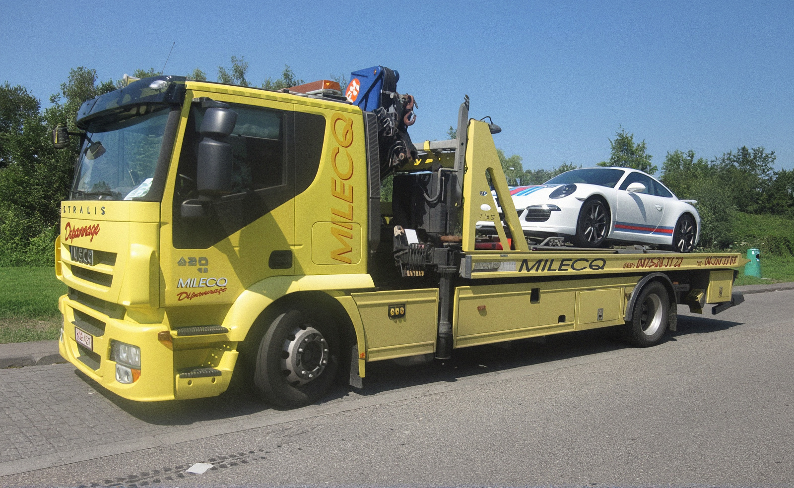 Camion de dépannage jaune Milecq transportant une Porsche 911 sur son plateau, région de Fléron